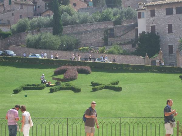 Assisi, gardener trimming hedges spelling Pax on the lawn