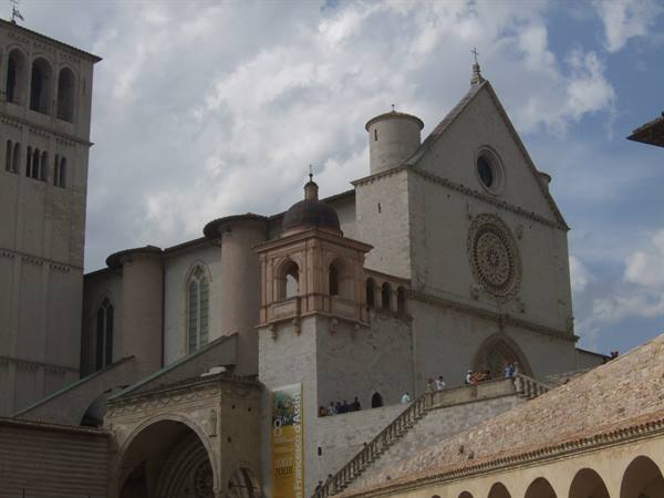 Basilica of San Francesco in Assisi, pale stone facade under drifting clouds