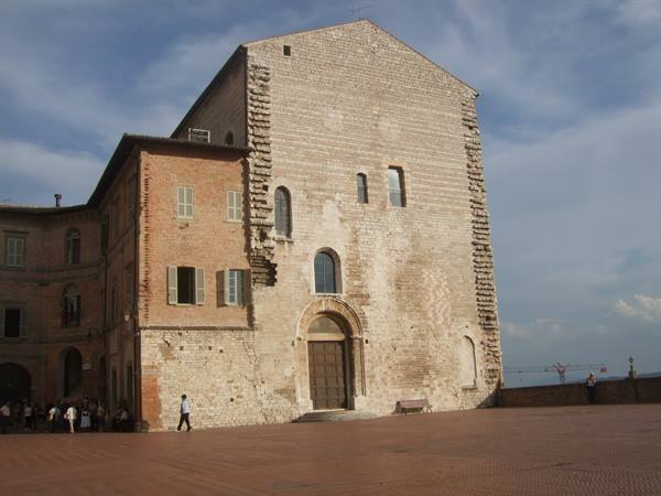 Piazza Grande in Gubbio, stone palace, tourists walk under cloudy sky