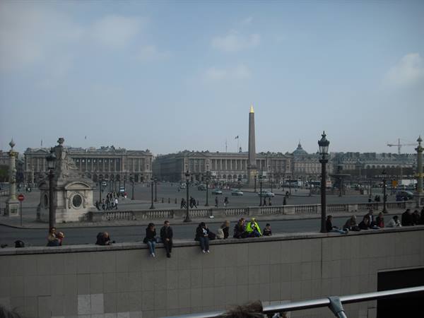 People sitting on a wall at Place de la Concorde with the Luxor obelisk
