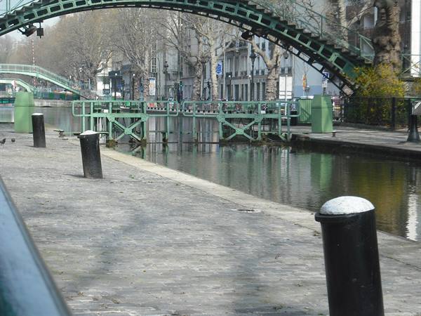 Green iron footbridge over Canal Saint-Martin, bollards and locks along the stone quay