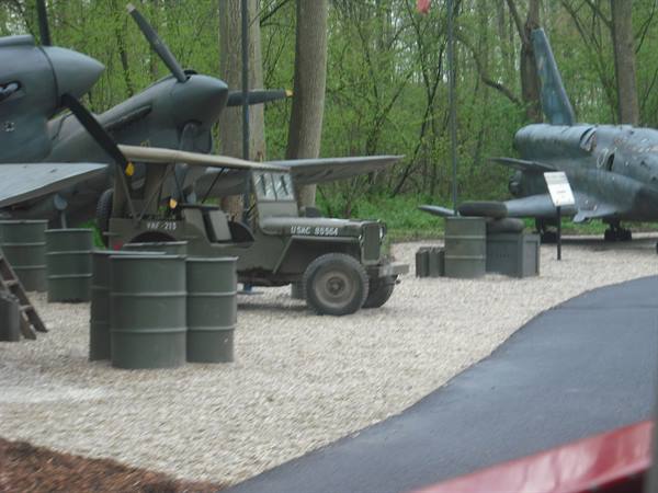 US Army military jeep among green barrels and vintage aircraft at museum
