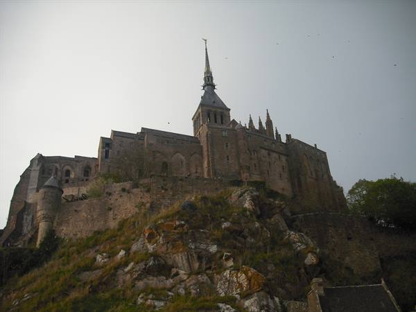 Mont Saint-Michel, stone abbey atop grassy rocky hill under grey sky