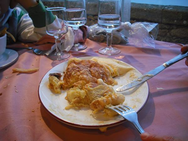 Half-eaten omelette on white plate, pink tablecloth, water glasses, natural light