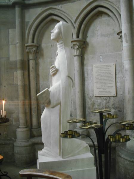Marble statue of a kneeling saint among metal candleholders inside a cathedral