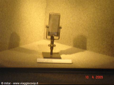 Vintage metal microphone displayed in a museum case, warm lighting