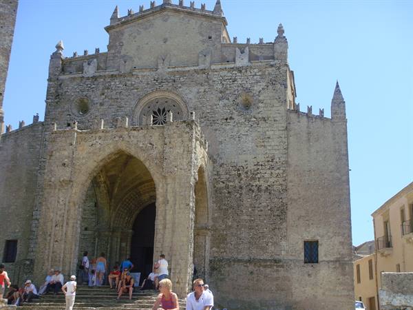 Tourists on the steps of Erice Cathedral, stone facade in bright sunlight