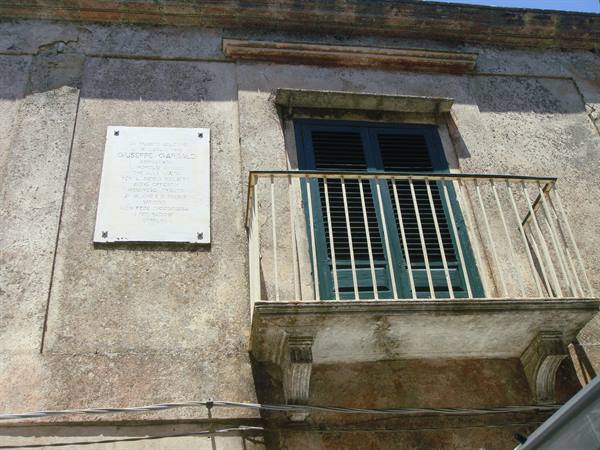 Stone balcony with white iron railing and green shutters on old facade with marble plaque