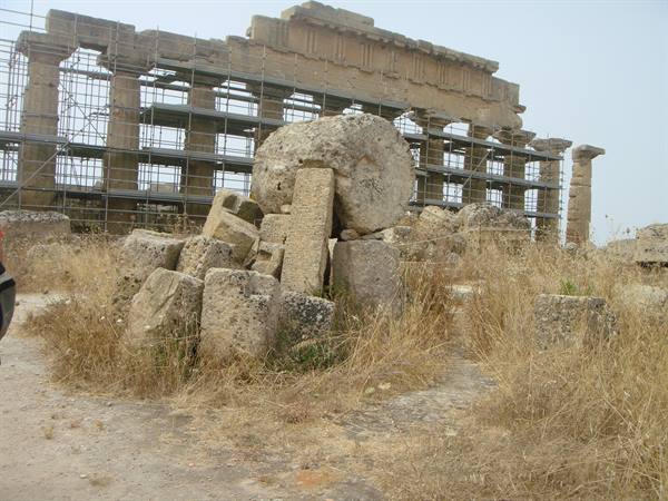 Selinunte temple ruins with scaffolding and fallen stone blocks among dry grass