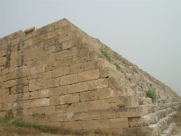 Monumental limestone block wall under a grey sky, with sparse grass