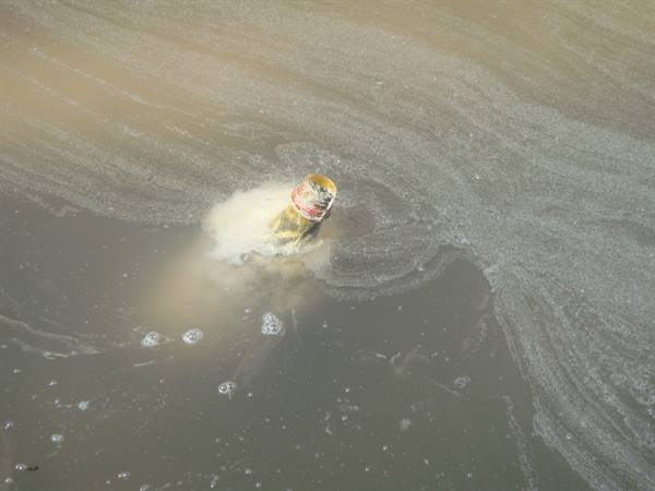 Discarded plastic bottle floating in murky foamy water
