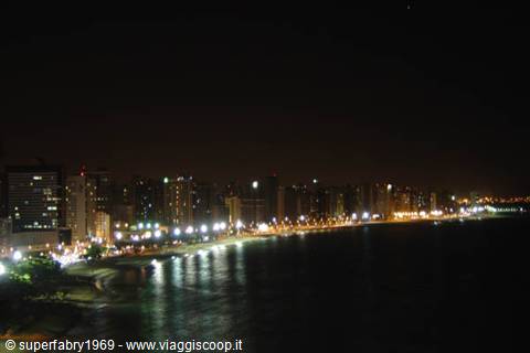 Illuminated high-rise buildings facing the dark sea at night in Fortaleza