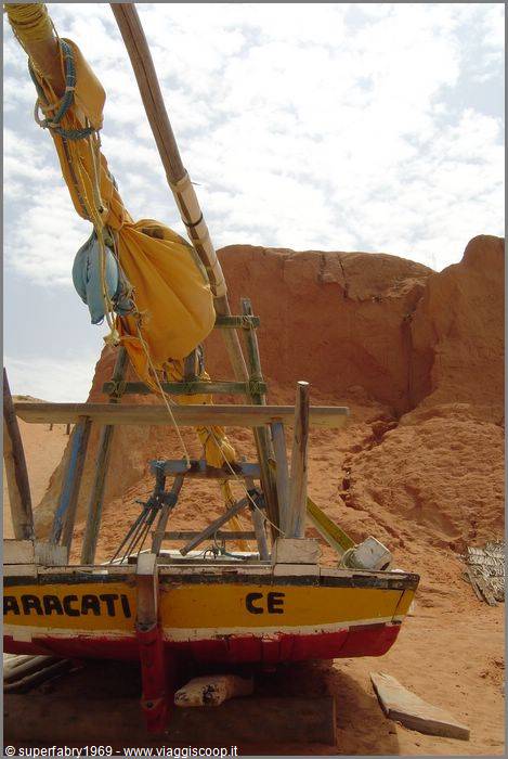 Wooden jangada boat beached on red sand, yellow sail tied, Aracati