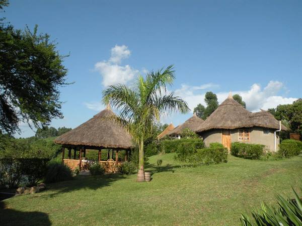 Thatched-roof bungalows and wooden gazebo on green lawn under blue sky