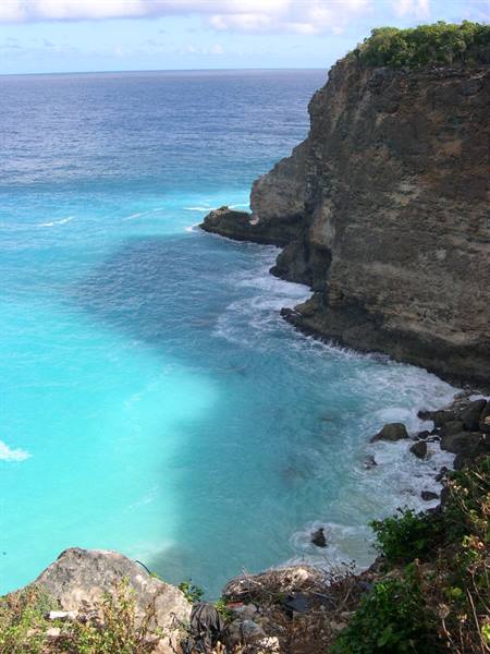 Limestone cliff over turquoise ocean, white waves crashing on rocks in sunlight