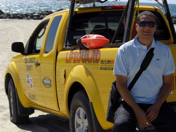 Man in sunglasses beside a yellow lifeguard pickup truck on Los Angeles beach