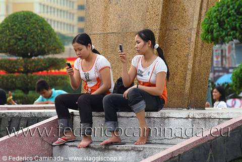 Two girls checking mobile phones, sitting on a granite fountain
