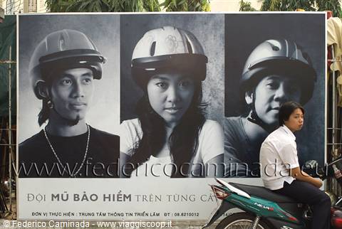 Road billboard with three helmet portraits, young rider passing by on scooter