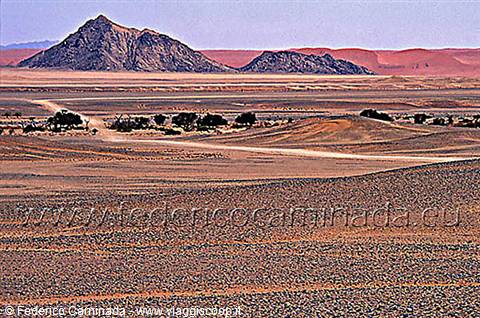 Red mountains and sandy tracks in the Namib desert under harsh light