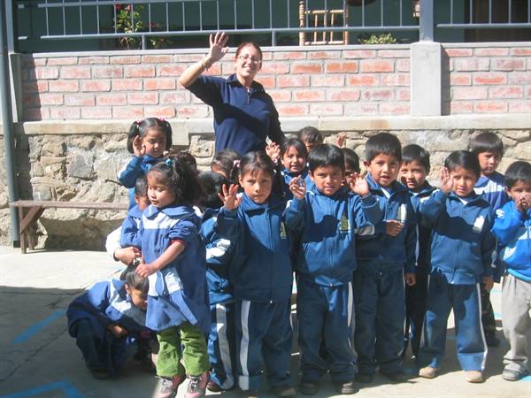 Teacher and children in blue uniforms wave in the school courtyard