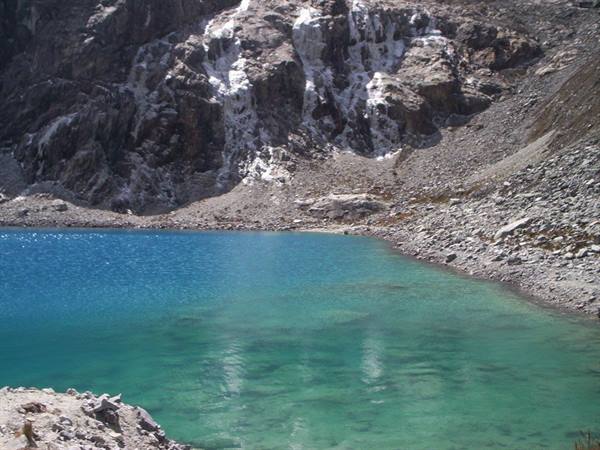 Turquoise alpine lake surrounded by scree and snow-patched rocks