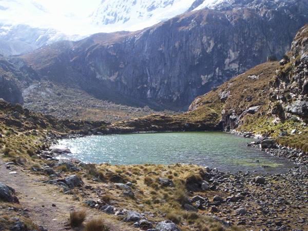 Green mountain lake surrounded by rocks and snowy peaks under sunlight