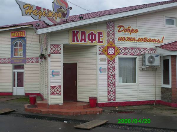 White and red wooden café with 'Nadezhda' sign, motel beside it, gray sky
