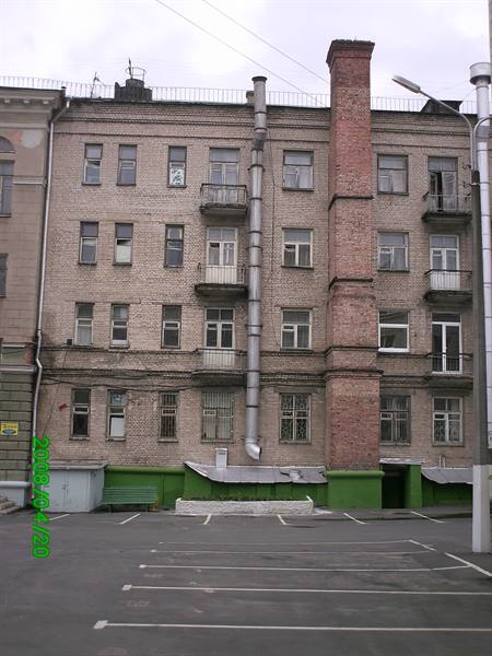 Old brick apartment building with chimney, pipes and empty parking lot