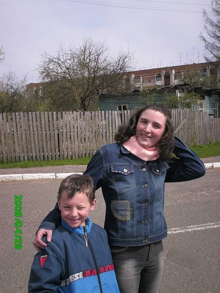 Smiling woman and boy posing on the road in front of a wooden fence