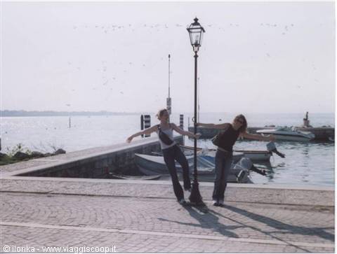 Two girls posing by a lamppost on the pier, moored boats and flying birds