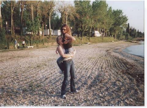 Two friends hugging on a pebble beach, campers and trees behind them