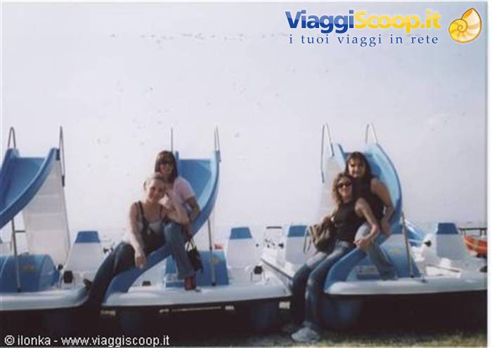 Four girls sitting on white and blue pedal boats with slides, sunny shore