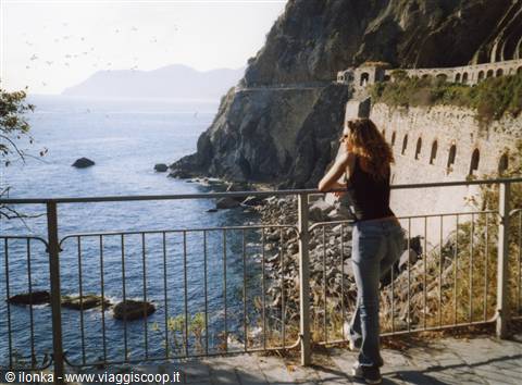Woman leaning on railing along Via dell'Amore, rocky cliffs and stone arches