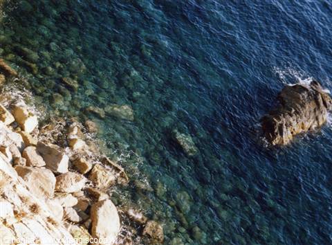 Light rocks on the shore, clear blue sea breaking over the stones