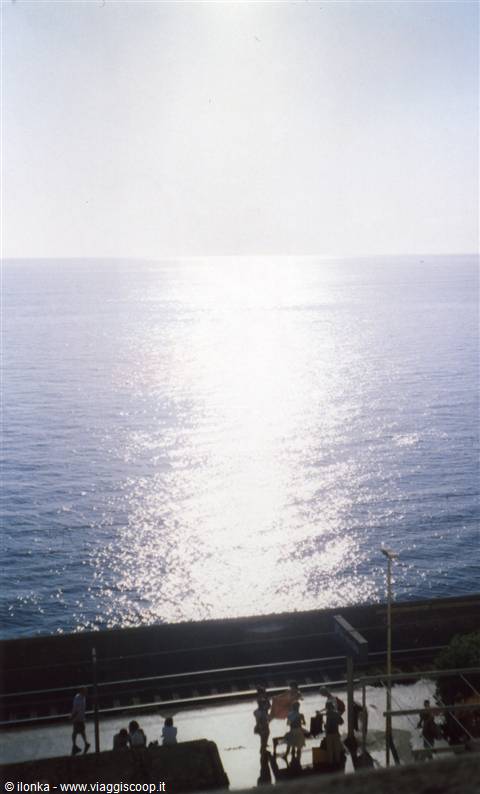 Sun reflected on the sea behind station tracks, people sitting on the platform