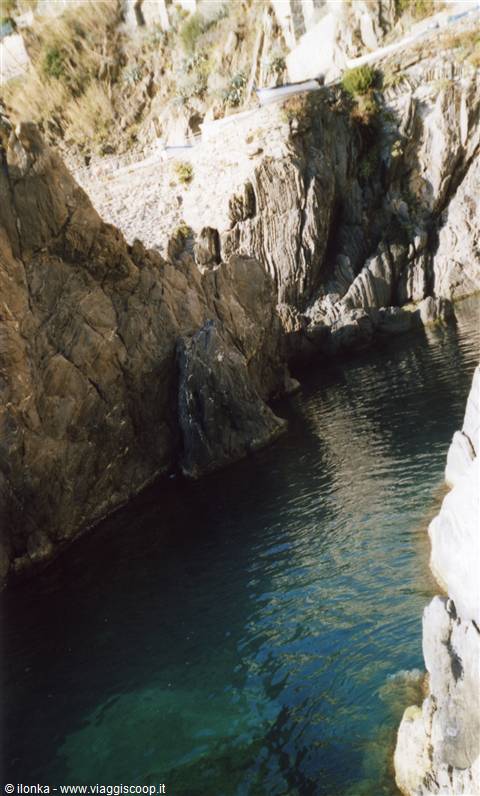 Green water cove between rocky cliffs, small boat near the shore