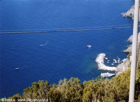 Deep blue sea with boats and a breakwater near the rocky coast