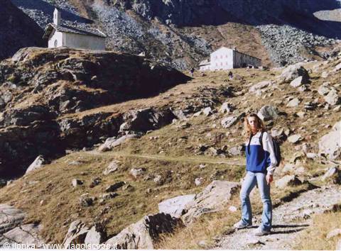Hiker with backpack on rocky trail, small church and refuge behind