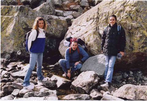Three girls with backpacks among granite boulders and mossy rocks near a stream