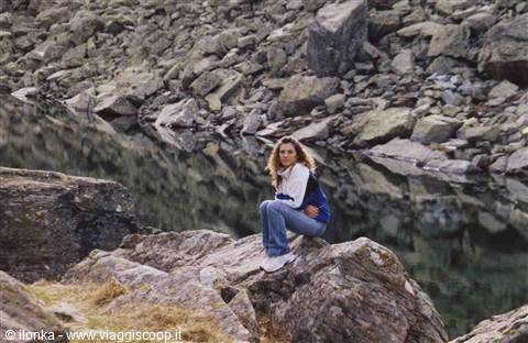 Girl sitting on a granite boulder beside an alpine rocky lake