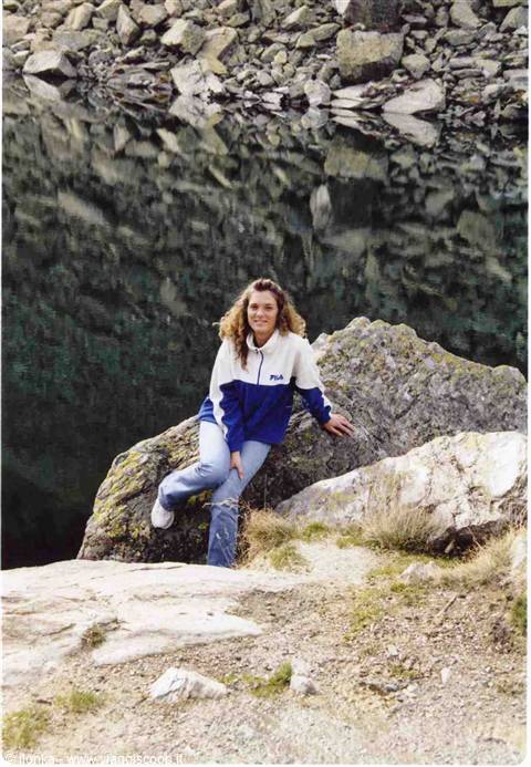 Woman sitting on a rock beside an alpine lake with stones reflected on water