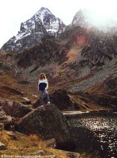 Woman standing on a rock beside an alpine lake, snowy peaks behind