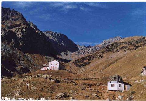 Stone mountain huts amid brown alpine meadows and rocky peaks, clear blue sky