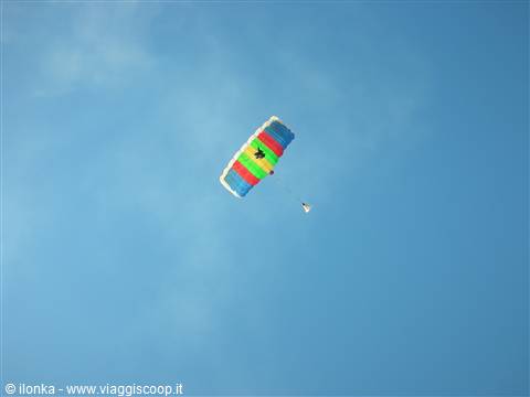 Parachutist descending through blue sky with green, red and blue canopy