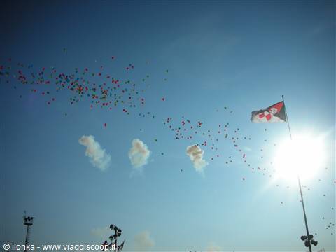 Multicolored balloons flying in the blue sky, flag waving next to the sun