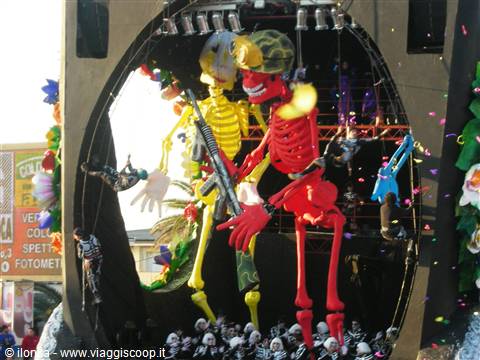 Viareggio Carnival: parade float with giant red and yellow skeletons, confetti falling