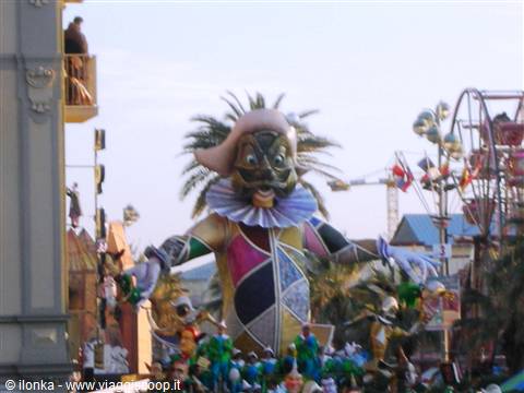 Harlequin carnival float with ruffled collar amid palms and fairground rides