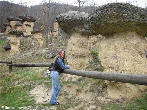 Woman leaning on a wooden fence beside large mushroom-shaped rock formations