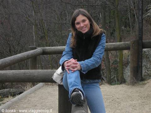 Smiling woman in jeans sitting on a wooden log among fences and bare woods