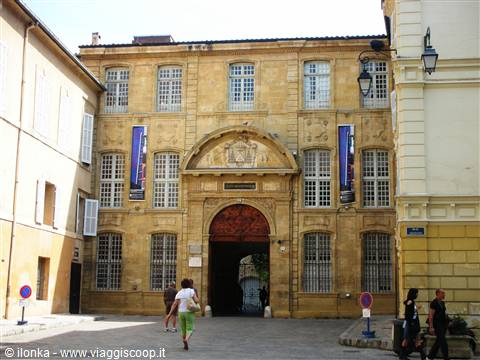 Pedestrian walking past the light stone facade of the old university building in Aix-en-Provence